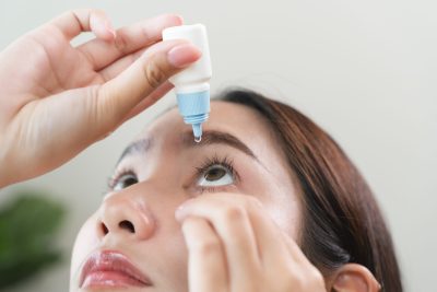 asian young woman using medical eye drops to treat dry eye and irritation.