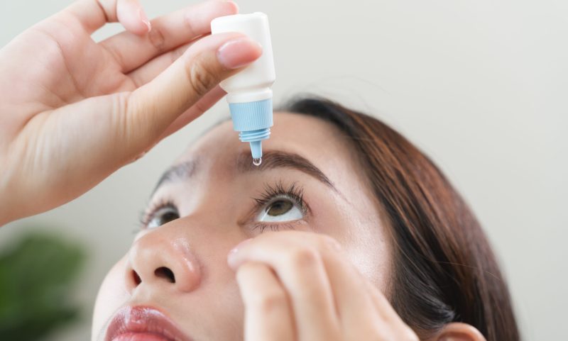 asian young woman using medical eye drops to treat dry eye and irritation.