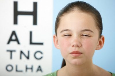 Girl squinting with eye chart in background --- Image by © Image Source/Corbis