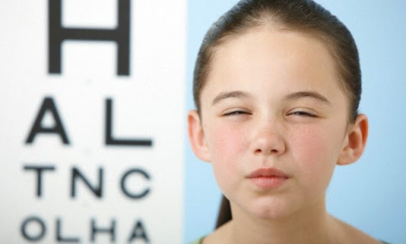 Girl squinting with eye chart in background --- Image by © Image Source/Corbis