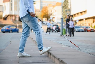 Young handsome blinded man walking with stick in town.