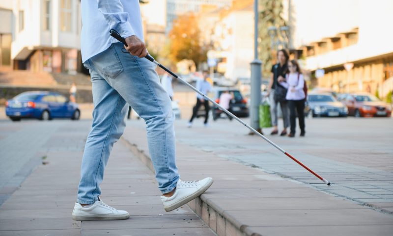 Young handsome blinded man walking with stick in town.